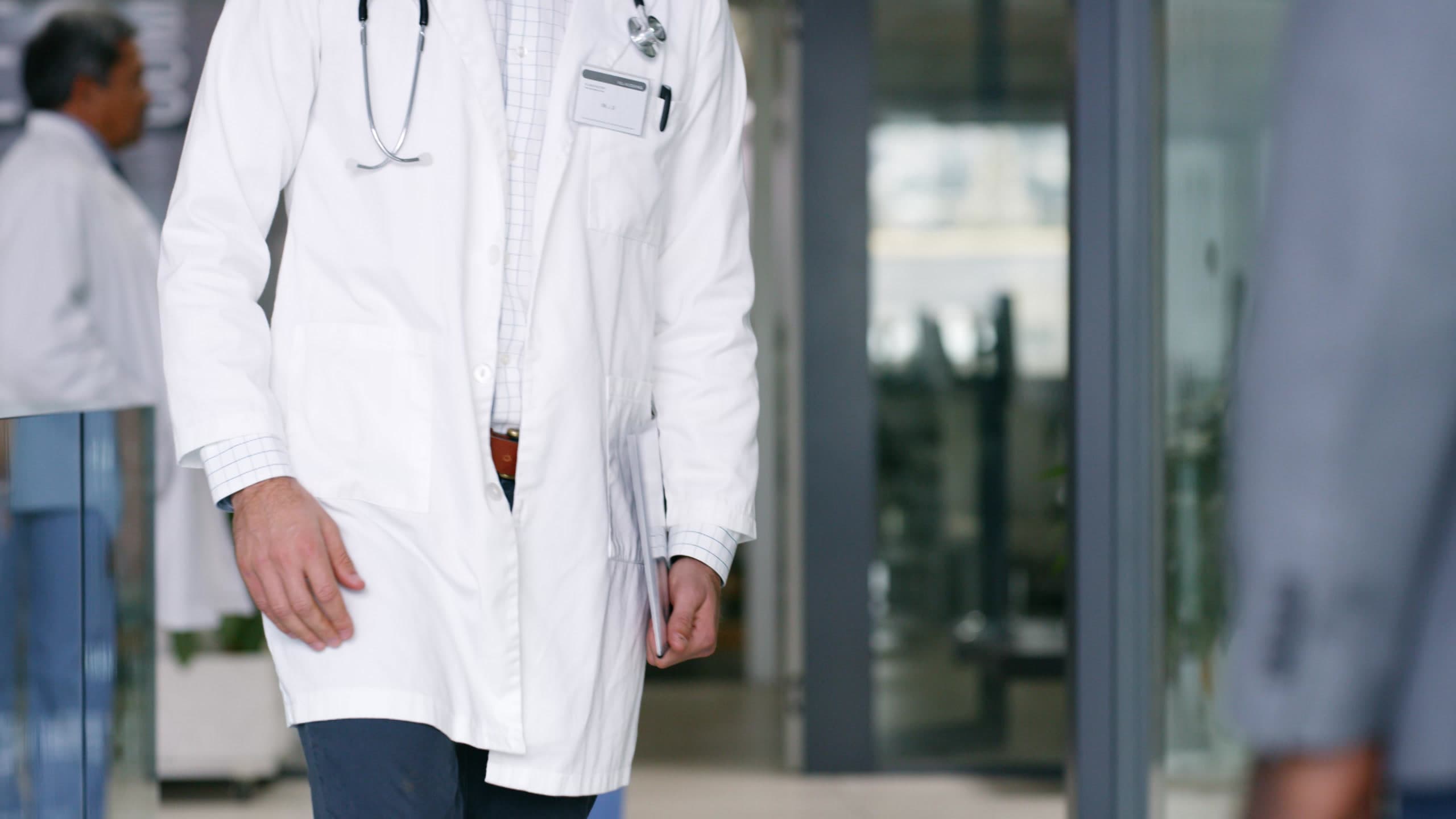 Physician in a white coat walking through a modern hospital corridor